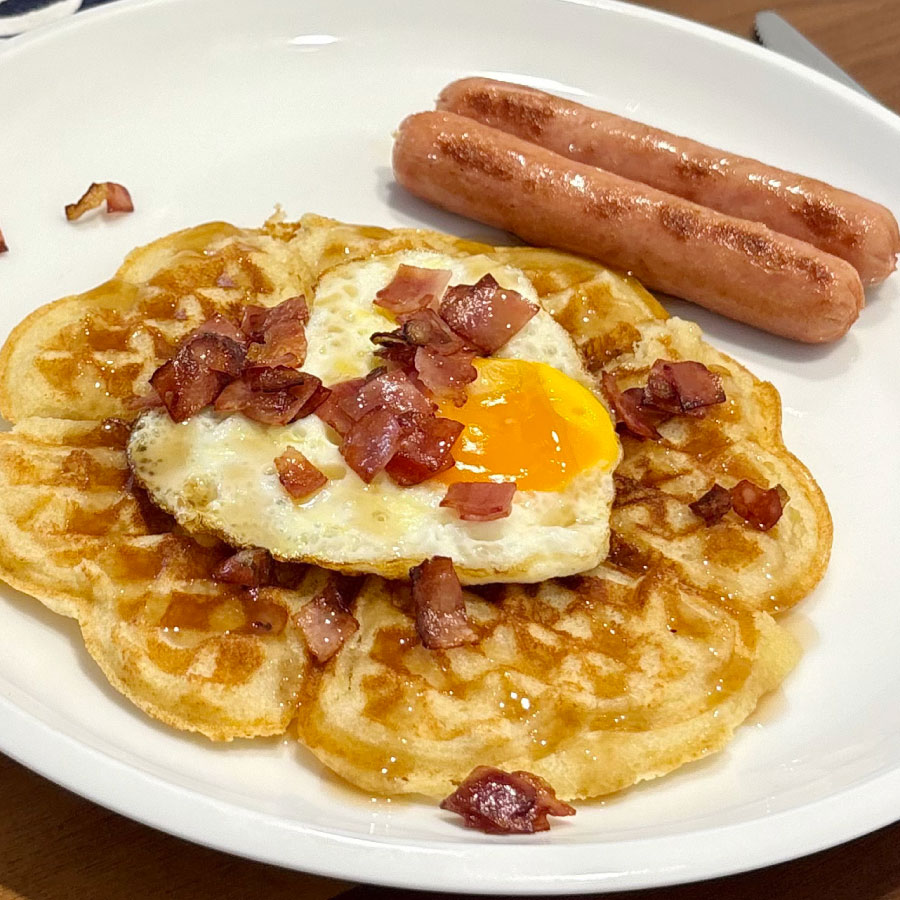 Waffle con huevo en forma de corazón, tocineta crocante y salchicha desayuno Fazán, acompañado con miel.