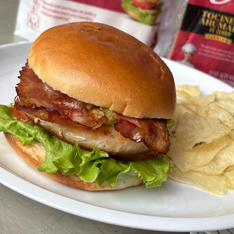 Hamburguesa de pollo con tocineta ahumada Fazán, lechuga, tomate y guacamole, servida con papas fritas.