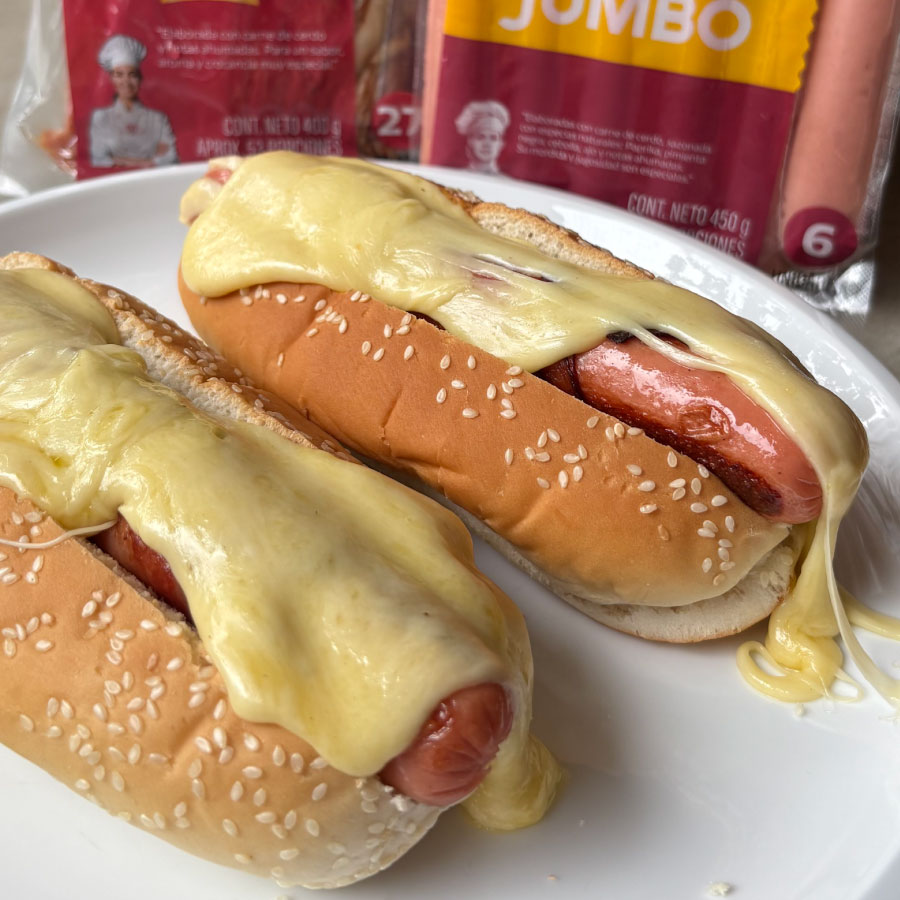 Perro hawaiano preparado con Salchicha Jumbo Fazán envuelta en tocineta ahumada, acompañado de una salsa cremosa de queso mozzarella y piña, servido en pan para perro caliente.