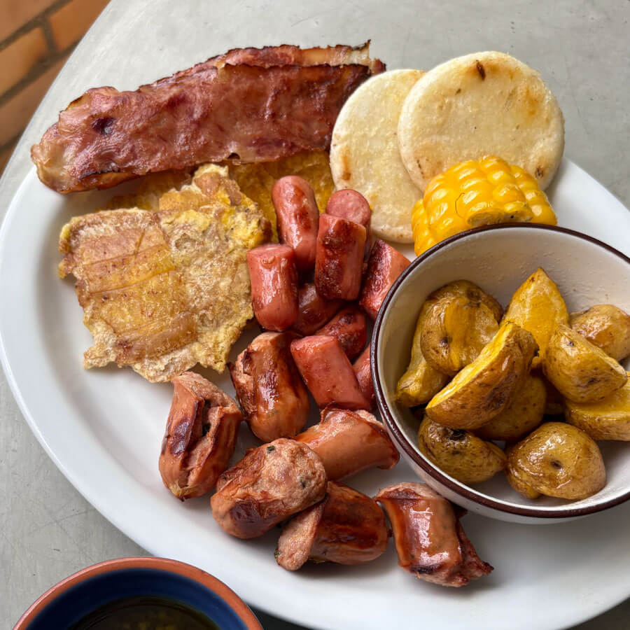 Parrillada paisa preparada con Salchicha Desayuno Premium, Chorizo Santarrosano y Tocineta Ahumada Fazán, acompañada de papas criollas, mazorca, arepas y patacones.