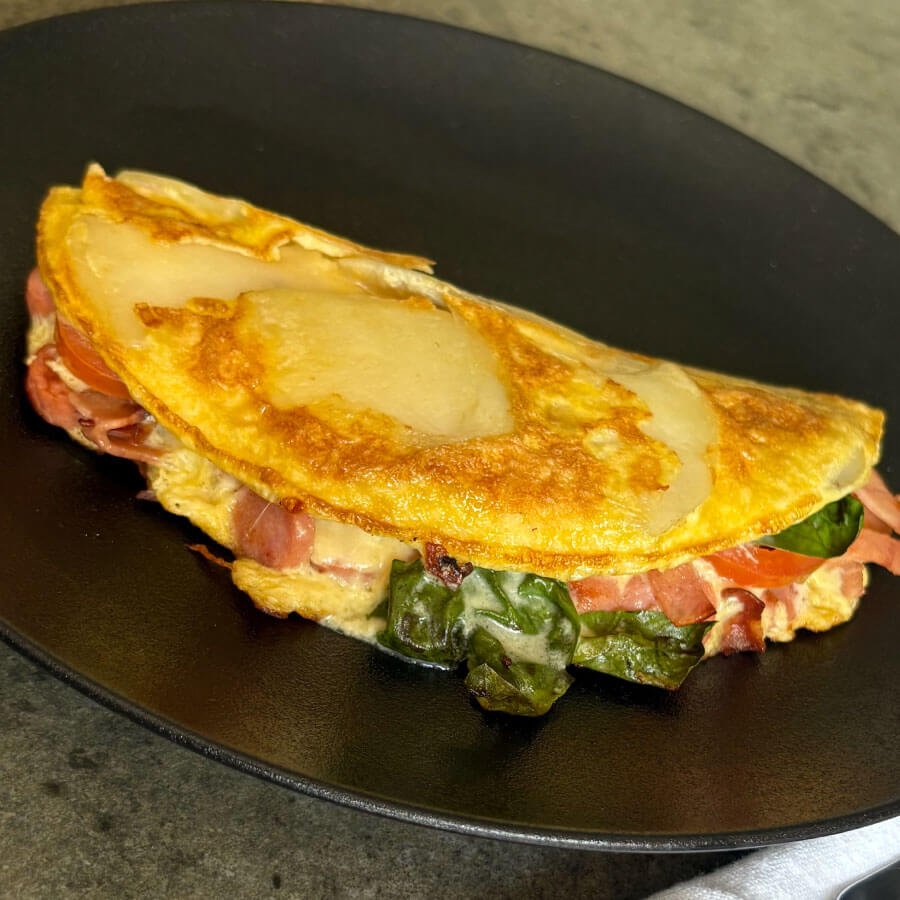 Tortilla de papa preparada con Salchicha Desayuno Premium y Tocineta Ahumada Fazán, queso mozzarella, tomate y albahaca, servida caliente como una receta fácil para compartir.