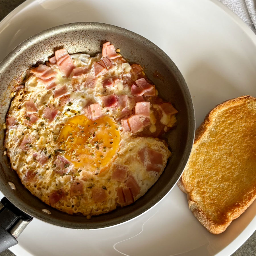 Huevos mediterráneos preparados con Jamón de Cerdo Premium Fazán, tomate, queso burrata o mozzarella y orégano, servidos con pan tostado.
